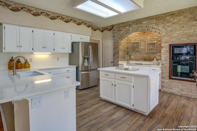 kitchen featuring white cabinetry, black appliances, hardwood / wood-style flooring, brick wall, and sink