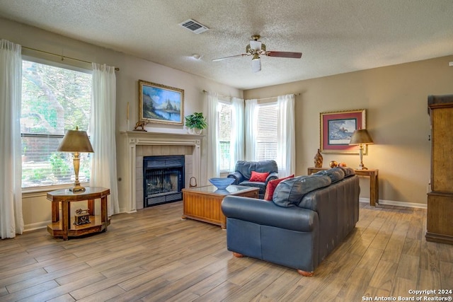 living room with ceiling fan, a fireplace, a textured ceiling, and hardwood / wood-style flooring