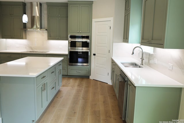 kitchen featuring wall chimney range hood, hanging light fixtures, sink, light hardwood / wood-style flooring, and appliances with stainless steel finishes