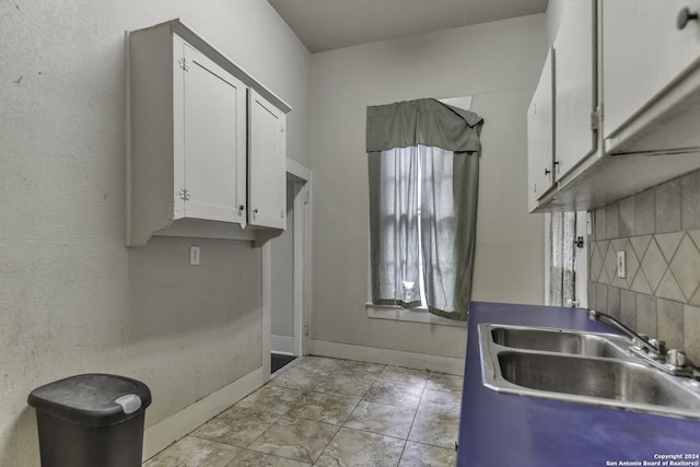 kitchen with baseboards, white cabinetry, and a sink