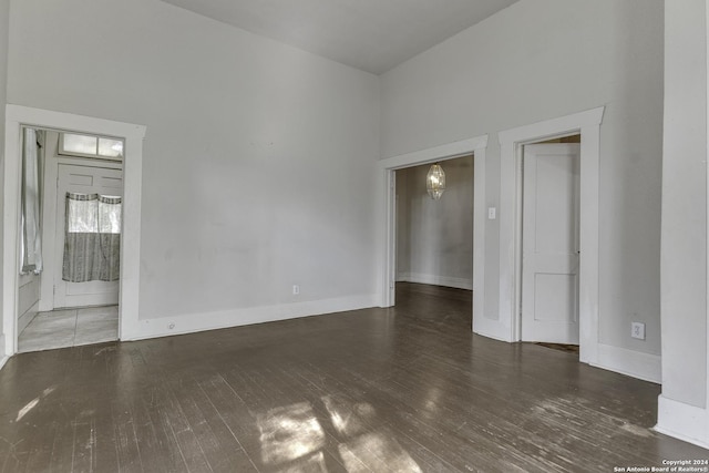 unfurnished room with baseboards, a high ceiling, a chandelier, and wood-type flooring