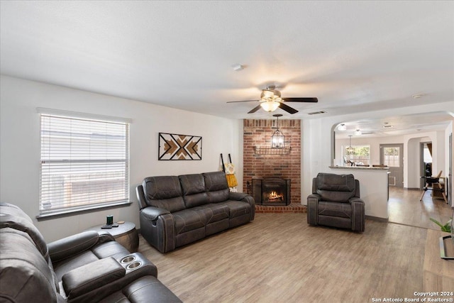 living room featuring light wood-type flooring, a brick fireplace, and ceiling fan