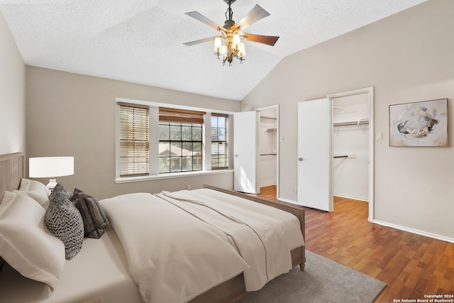 bedroom with hardwood / wood-style flooring, a walk in closet, vaulted ceiling, and a textured ceiling