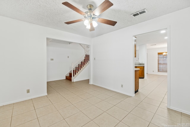 tiled empty room featuring ceiling fan with notable chandelier and a textured ceiling