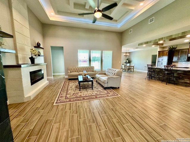 living room with a towering ceiling, a tiled fireplace, light wood-type flooring, and ceiling fan