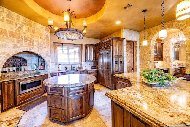 kitchen with a center island, hanging light fixtures, a raised ceiling, wall oven, and light stone countertops