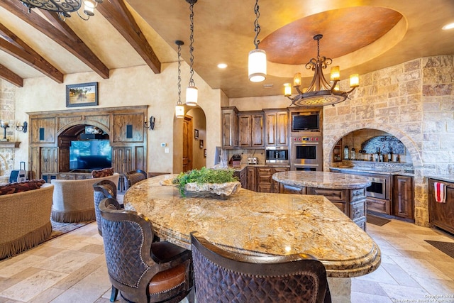 kitchen featuring an inviting chandelier, hanging light fixtures, double oven, a center island, and light stone countertops