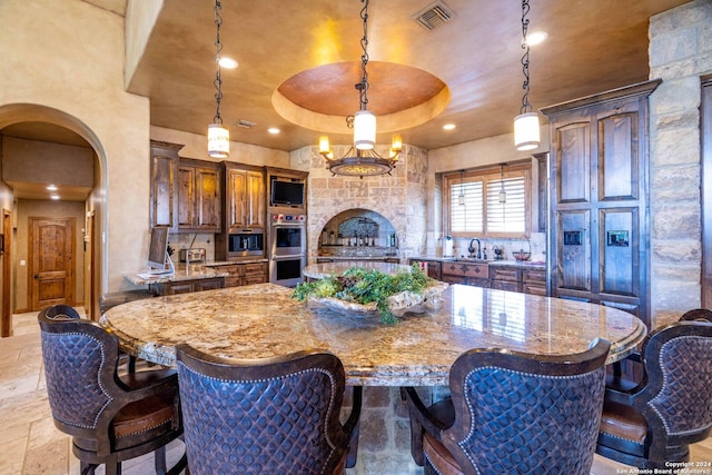 kitchen featuring pendant lighting, a tray ceiling, light stone countertops, stainless steel double oven, and a spacious island