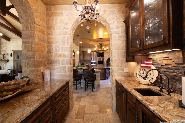 kitchen featuring dark brown cabinetry, sink, a chandelier, hanging light fixtures, and light stone countertops