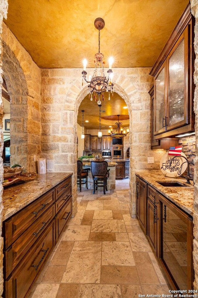 kitchen featuring stainless steel oven, a notable chandelier, light stone counters, and decorative light fixtures