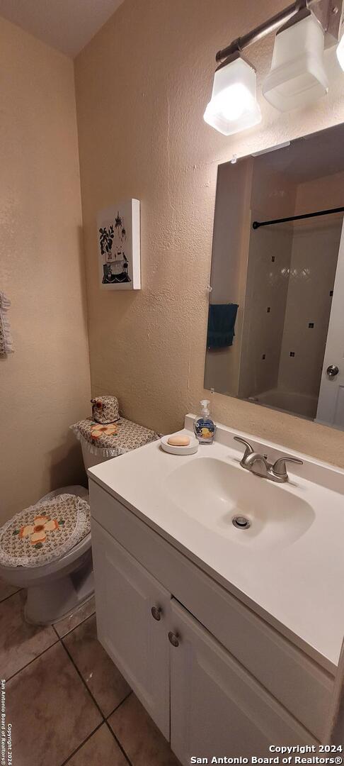 bathroom featuring toilet, a textured wall, vanity, and tile patterned floors