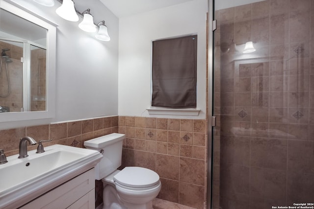 bathroom with a shower with door, vanity, tile walls, and toilet