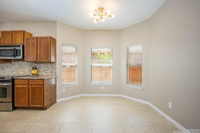 kitchen featuring light tile patterned flooring, decorative backsplash, light stone counters, stainless steel appliances, and an inviting chandelier