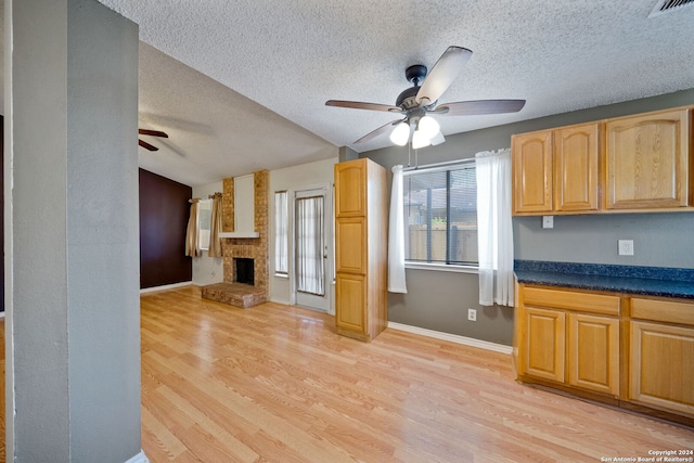 kitchen with ceiling fan, light hardwood / wood-style flooring, a textured ceiling, and a brick fireplace