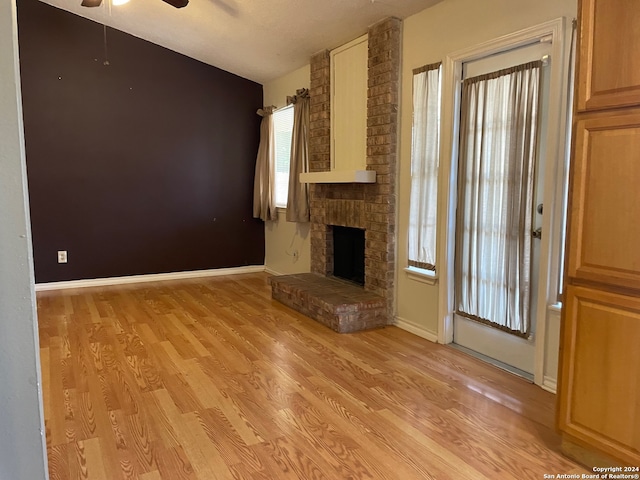 unfurnished living room featuring brick wall, light hardwood / wood-style flooring, a fireplace, and ceiling fan