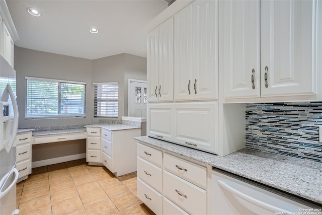 kitchen featuring dishwasher, built in desk, light stone countertops, light tile patterned floors, and white cabinetry