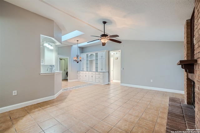 unfurnished living room featuring ceiling fan with notable chandelier, a brick fireplace, light tile patterned flooring, and vaulted ceiling with skylight