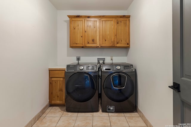 clothes washing area with light tile patterned floors, washing machine and clothes dryer, and cabinets