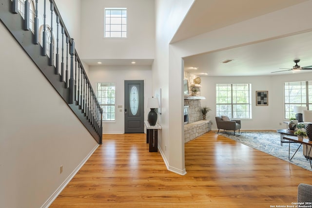 entrance foyer featuring a stone fireplace, light hardwood / wood-style floors, a high ceiling, and ceiling fan