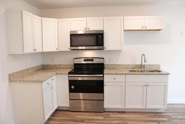 kitchen with light stone countertops, sink, stainless steel appliances, light hardwood / wood-style floors, and white cabinets