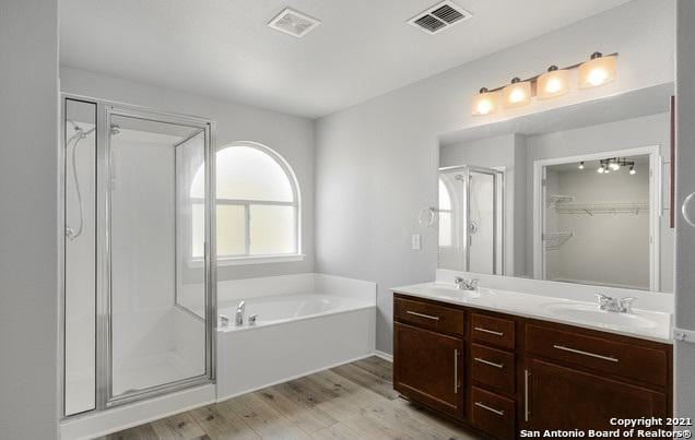 bathroom with a stall shower, wood finished floors, a sink, and double vanity