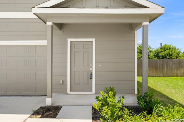 property entrance with a garage, a yard, board and batten siding, and fence