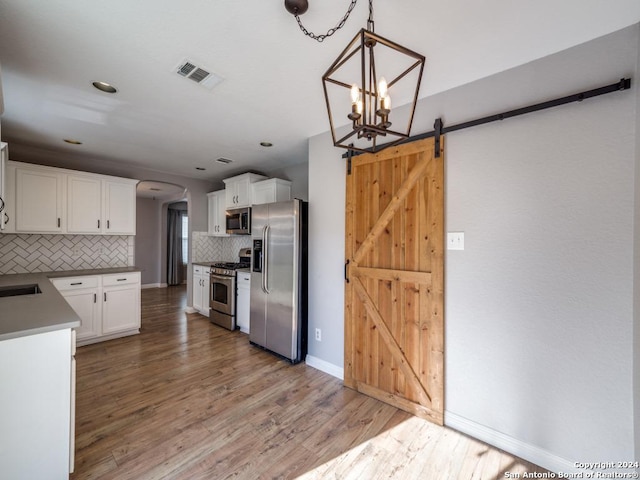 kitchen featuring a barn door, hardwood / wood-style floors, appliances with stainless steel finishes, pendant lighting, and white cabinets