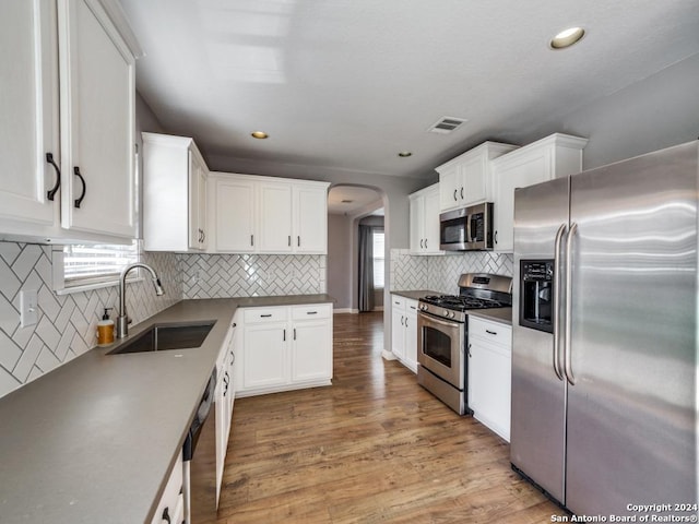 kitchen featuring appliances with stainless steel finishes, white cabinetry, sink, backsplash, and light hardwood / wood-style flooring