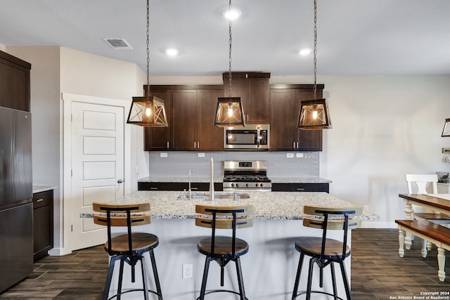 kitchen with pendant lighting, decorative backsplash, a kitchen island with sink, stainless steel appliances, and dark brown cabinets