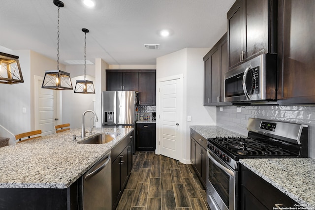 kitchen with sink, appliances with stainless steel finishes, tasteful backsplash, dark brown cabinetry, and an island with sink