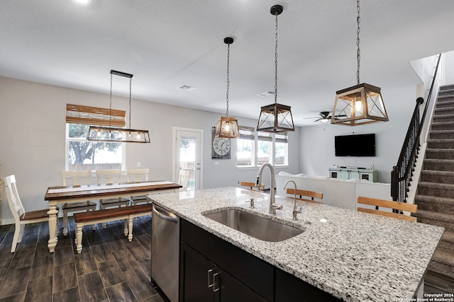 kitchen with pendant lighting, dishwasher, sink, light stone counters, and a center island with sink