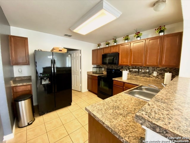 kitchen with light tile patterned flooring, decorative backsplash, sink, and black appliances