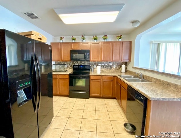 kitchen featuring tasteful backsplash, light tile patterned floors, kitchen peninsula, black appliances, and sink