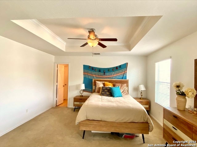 bedroom with ceiling fan, light carpet, crown molding, and a tray ceiling