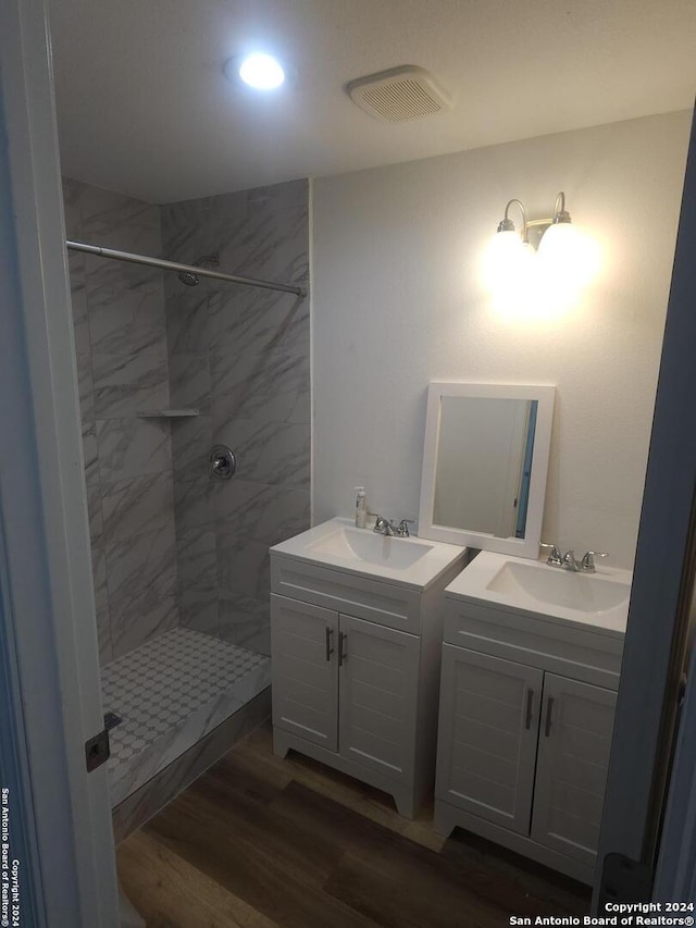 bathroom with tiled shower, hardwood / wood-style flooring, and double sink vanity