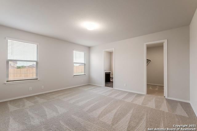 unfurnished bedroom featuring ensuite bathroom, a walk in closet, light carpet, and a closet