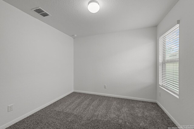 unfurnished room with a textured ceiling and dark carpet