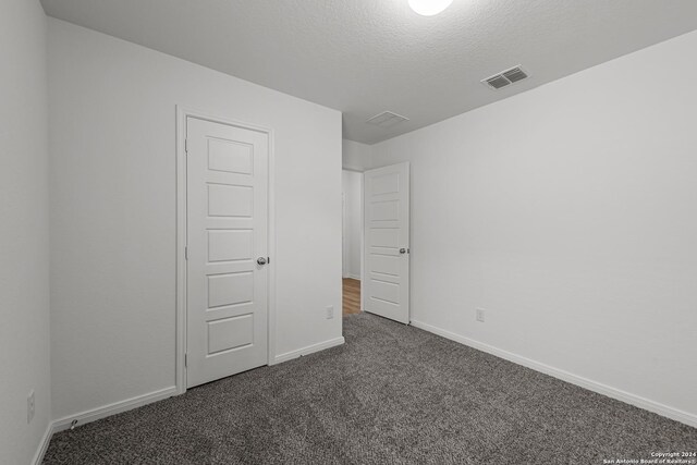 unfurnished bedroom featuring a textured ceiling and dark colored carpet