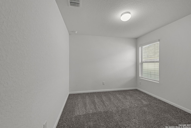 spare room with a textured ceiling and dark colored carpet