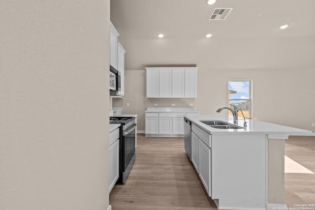 kitchen with white cabinetry, stainless steel appliances, sink, a kitchen island with sink, and light hardwood / wood-style flooring