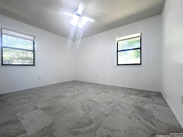 empty room with ceiling fan, plenty of natural light, and a textured ceiling