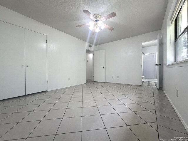 unfurnished bedroom featuring ceiling fan, a closet, a textured ceiling, and light tile patterned flooring