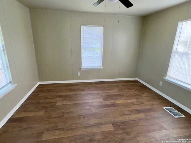 empty room with a wealth of natural light, ceiling fan, and dark wood-type flooring