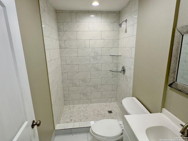 bathroom featuring vanity, tiled shower, tile patterned flooring, and toilet