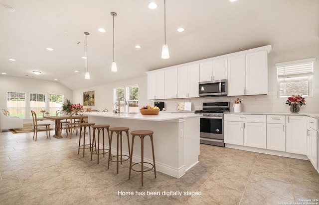 kitchen featuring pendant lighting, lofted ceiling, stainless steel appliances, and a center island with sink