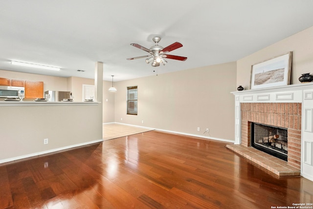 unfurnished living room featuring a brick fireplace, hardwood / wood-style floors, and ceiling fan