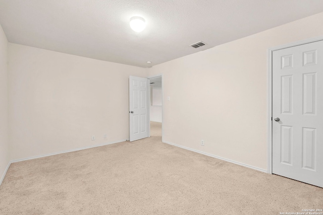 spare room featuring light colored carpet and a textured ceiling