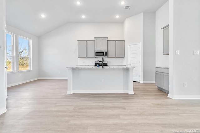 kitchen featuring light hardwood / wood-style flooring, gray cabinets, vaulted ceiling, and light stone counters