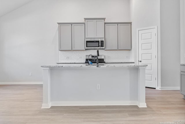 kitchen with light stone countertops, tasteful backsplash, gray cabinetry, stainless steel appliances, and a kitchen island with sink