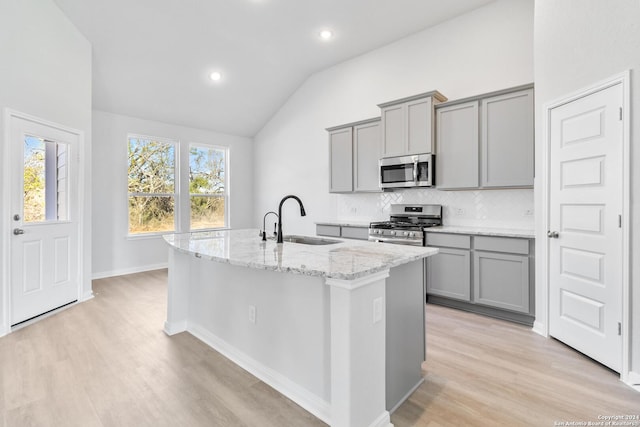 kitchen with sink, an island with sink, lofted ceiling, and appliances with stainless steel finishes